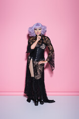 full length view of drag queen in black lace dress showing hush sign on pink.