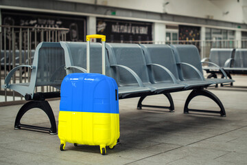 A large blue and yellow suitcase on wheels sits on the floor in a modern airport terminal. Ukrainian refugees are leaving the country.