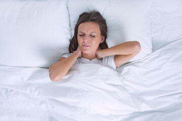 Woman in bed suffering from neck pain in the morning after sleeping on uncomfortable pillow. Pain in neck, cervical chondrosis or osteochondrosis