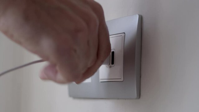 A hand connecting a usb cable to a jack on the wall