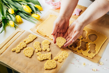 Woman cutting pastry dough into Easter egg shape while making sugar cookies. Holidays baking. Top view