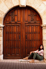 beautiful young indian woman sat over a wooden church door, vertical copy space