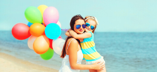 Happy mother and little girl child with colorful balloons on beach over sea background