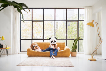 Two unrecognizable women with animal mask bear panda lying at sofa home - Beautiful living room...