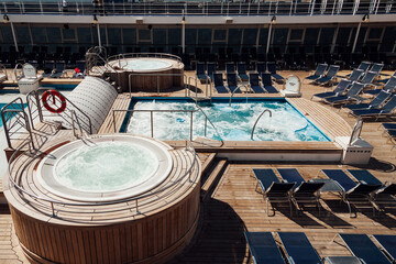 View of a swimming pool and jacuzzi of a cruise ship with no people on board. Deck of a luxury ship with chairs for sunbathing. . High quality photo horizontal