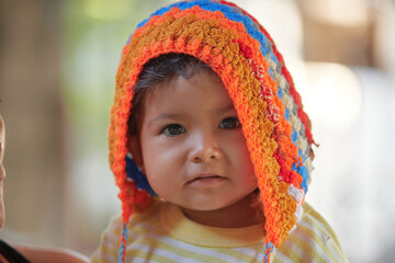 Happy Latin babe, in natural light. Happy family. Face of a Mexican girl with a colorful hat in her mother's arms. Expressions on the face.