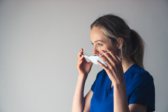 Young pensive caucasian female surgeon putting on or taking off her face mask. High quality photo