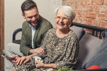 happy smiling laughing short-haired grandmother sits on a couch and looks at old pictures with her...