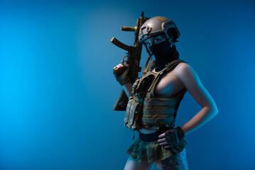 Fototapeta na wymiar a naked girl soldier in a bulletproof vest and helmet, armed with an automatic rifle, in military clothes on a blue background