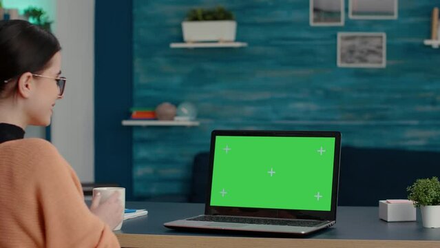 Young student looking at green screen on laptop computer, studying for online class lesson at home. Woman using isolated template with blank chroma key and mockup copy space on computer.