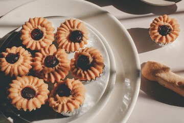 Cookie with red jam with coffee  in morning light from window. Coffee break or tea Time. Home breakfast, afternoon tea. Served on plate. Selective focus