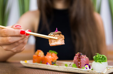 Woman eating delicious sushi, closeup on chopsticks.