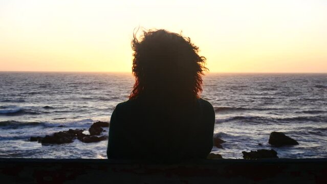 Una mujer pensativa frente al mar en un atardecer de verano.