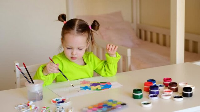 A child paints a drawing with watercolor paints at a desk in the children's room. A child prepares a drawing on the topic of autism awareness