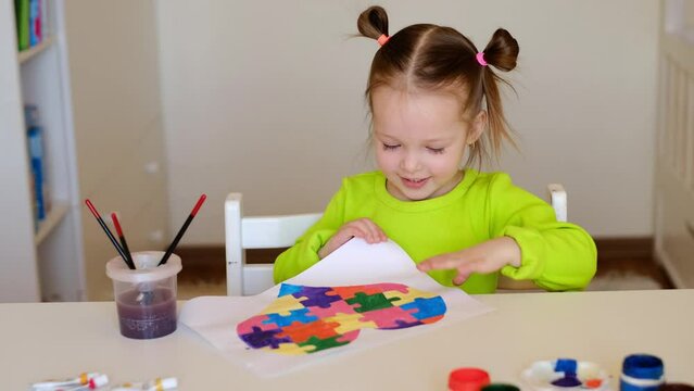 Little happy girl demonstrates her drawing of a heart card with puzzles for children suffering from autism. The child learns to give a helping hand, tolerance and respect for other people. Autism Day