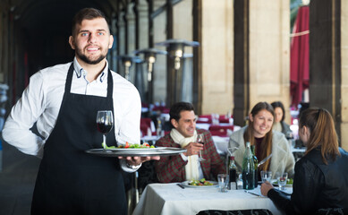 Obraz premium Smiling waiter holding tray at restaurant with customers his behind
