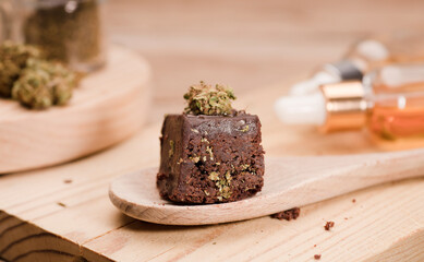 Chocolate cupcake muffins with cannabis buds in wooden spoon, oil pot and cooking jars. Marijuana hemp in food dessert. Chocolate herb muffins cooking. Marijuana cake on a brown wooden table.