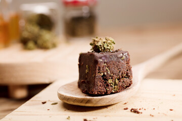 Chocolate cupcake muffins with cannabis buds in wooden spoon, oil pot and cooking jars. Marijuana hemp in food dessert. Chocolate herb muffins cooking. Marijuana cake on a brown wooden table.