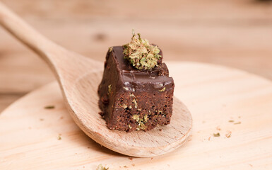 Chocolate cupcake muffins with cannabis buds on wooden spoon. Marijuana hemp in food dessert. Chocolate herb muffins cooking. Marijuana cake on a brown wooden table.