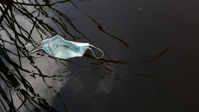 Detalle de una mascarilla sanitaria saliendo a flote del fondo de un r&iacute;o.