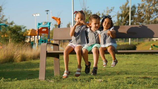 Ni&ntilde;os Felices amigos hermanos combinados vestidos igual amistad divertidos disfrutando sentados jugando en el parque en una banca al aire libre en juegos infantiles 