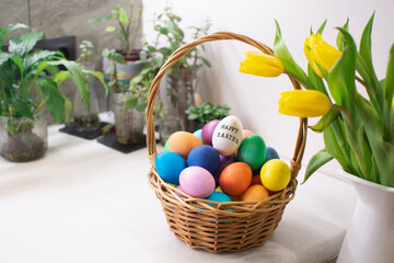 Colorful Easter eggs in wicker basket on table in kitchen interior with tulips