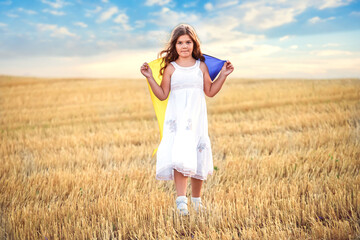 Pray for Ukraine. girl with the flag of Ukraine without war. A child holds a yellow-blue Ukrainian flag and walks through a field of wheat. Grain harvest in an agrarian country