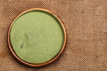 supergreens powder in a wooden bowl on textured burlap . Healthy food concept