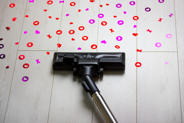 Vacuum cleaner cleans white floor from scattered heart-shaped confetti from poppers cannons....
