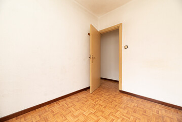 Room with white painted walls, parquet flooring and light brown painted door