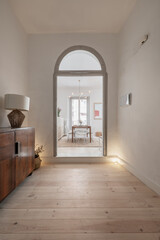 Entrance hall of a house with neo vintage decoration with large wooden lockers, doors with gray semicircular arches and large light pine wood slat floors with a dining table in the background
