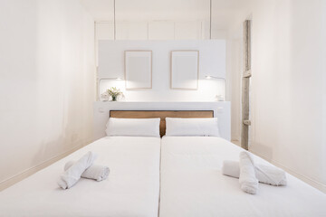 Fototapeta na wymiar Bedroom with double beds joined together, white bedding, towels rolled up on the beds, and white décor in a vacation rental home