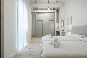 Bedroom with double beds joined together, white bedding, towels rolled up on the beds, and white decor with hardwood floors, gray sliding closet doors, and exposed beams in a vacation rental home