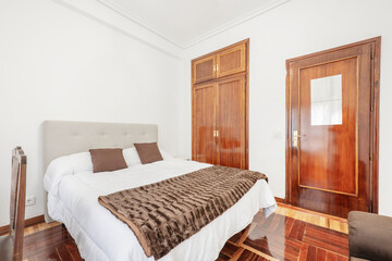 Bedroom with king-size bed and headboard upholstered in fabric, fitted wardrobes with mahogany-colored wooden doors that match the parquet floors