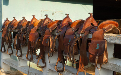 leather western trail saddles with saddle bags and horns lined up on white fence in rural Cuba...