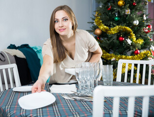 Portrait of attractive young woman preparing table for celebration of Christmas at home