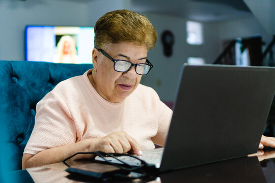 older latina woman using a laptop computer. close up, wearing glasses with protection, going blind she can hardly see.
