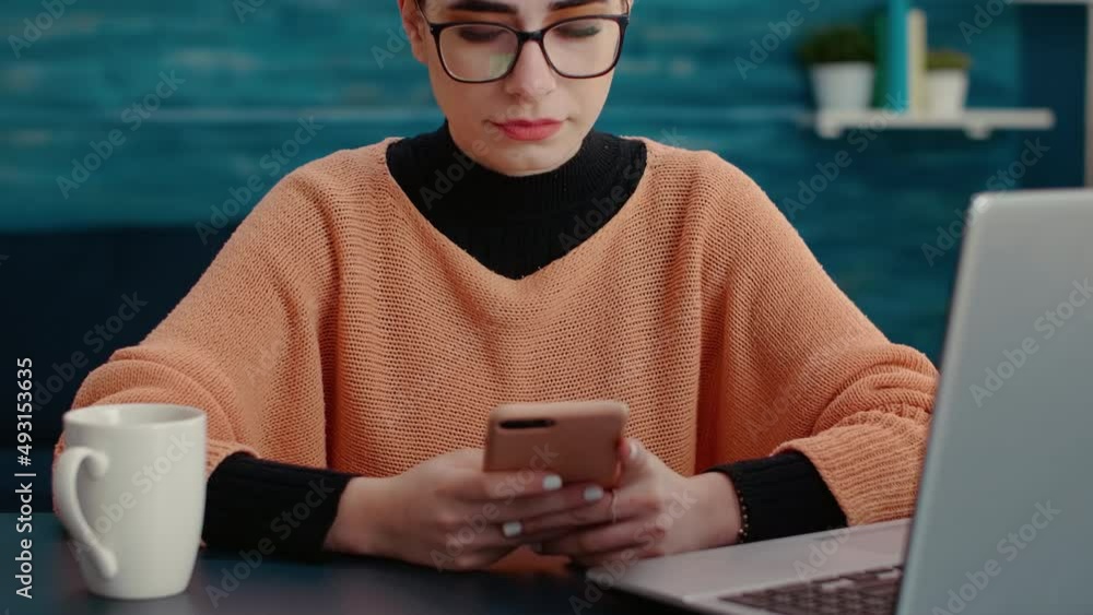 Poster portrait of female student using smartphone to browse internet and smiling at camera in living room.