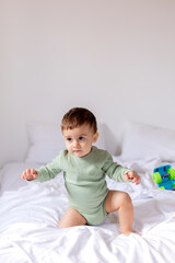 Naklejka premium baby in a green cotton bodysuit is sitting on a white bed with a colored toy car. child is playing