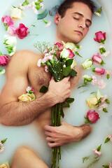 Its not a relaxing bath if the water is not milky. High angle shot of a handsome young man holding a bouquet while lying in a bathtub full of milky water and flower petals at home.