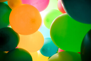 Colorful balloons all over the frame, lying one next to the other.  Many colored balloons looking like colored balls