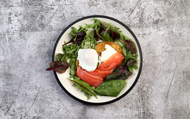 Hash browns with smoked salmon, poached egg and herbs on a round plate on a dark gray background. Top view, flat lay