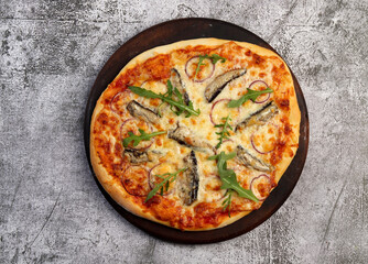 Homemade Sardine Pizza on a round wooden cutting board on a dark grey background. Top view, flat lay