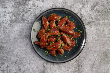 Honey Glazed Chicken Wings with sesame seeds and herbs on a round plate on a dark gray background. Top view, flat lay