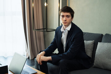 caucasian businessman working with laptop, wear suit, sit on sofa, looking at camera. Young man work business with home office background and copy space