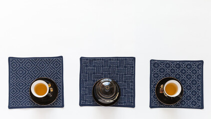 Top view of tea table with black cups of green tea and crystal sugar on blue napkins embroidered by...