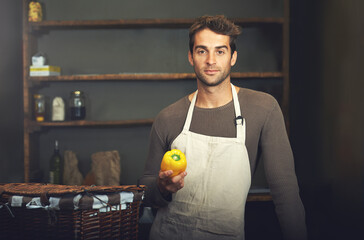 Hes a pro in the kitchen. Shot of a young man holding a yellow pepper in his kitchen.