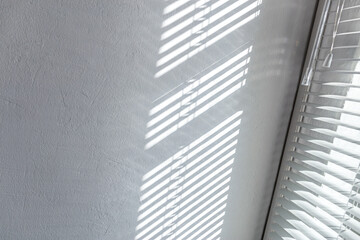 sunlight reflections from the window blinds on the white plaster wall