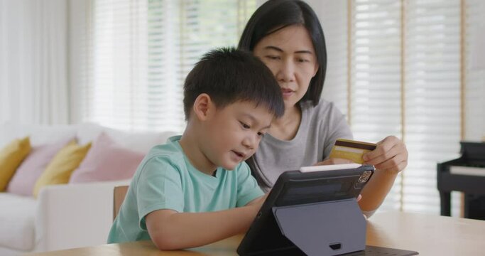 Young boy alpha gen z little kid help mom pay school charge tuition term fee or tax bill on web social media app relax smile at home table. Asia people happy playful fun buy gift card on online shop.
