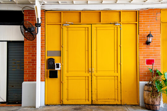Front view of closed Cafe shop and Restaurant design. Modern Loft metal closed doors yellow, orange brick wall, and green plastic plant bush.